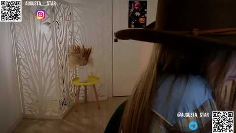 Media: Video of a dimly lit room with a person wearing a brown cowboy hat, standing behind a white screen with tree-like patterns.