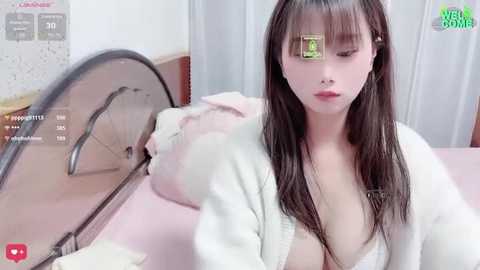 Media: A video of an Asian woman with long black hair, wearing a white robe, lying on a pink bed, eyes closed, in a bedroom with a metal bed frame.