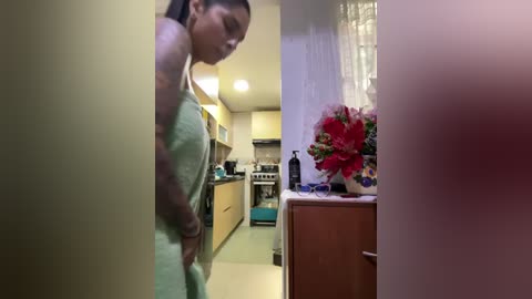 Media: A video of a tattooed woman in a kitchen, wearing a green apron, with a blurred background of a small, cozy space.