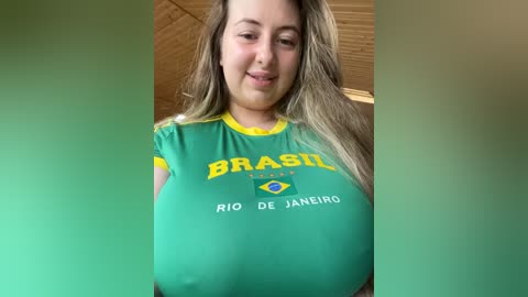 Media: A video of a young woman with long, light brown hair wearing a tight, green Brazil soccer jersey, showcasing her large breasts. The background shows a wooden ceiling and walls.