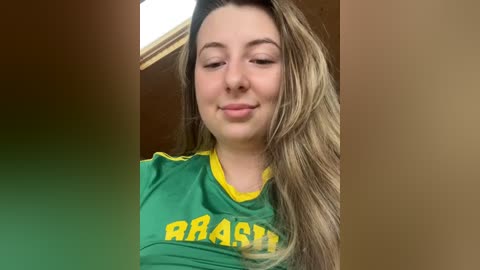 Media: Video of a young woman with long, light brown hair, fair skin, and a slight smile, wearing a green sports jersey with yellow trim and the word \"Brasil\" in yellow.