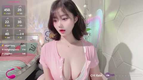 Media: A video of a young Asian woman with fair skin and short black hair, wearing a low-cut pink blouse, standing in a brightly lit room with colorful decor.