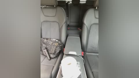 Media: Video of a car interior showing a folded black plastic bag and a cup on the center console between two front seats, all in a gray-toned, minimalist setting.