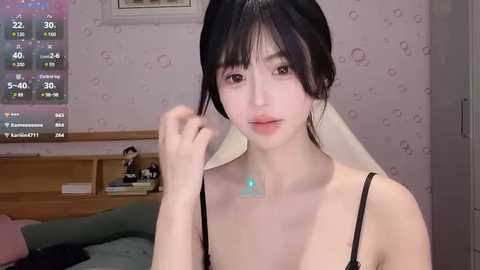 Media: A video of an Asian woman with fair skin, black hair, and a slender build, wearing a black strapless top, adjusting her hair in a bedroom with a TV displaying weather information.