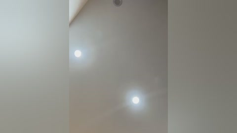 Media: Video of a minimalist, modern ceiling with three evenly spaced recessed lights casting soft, diffused light against a smooth, off-white surface. The image has a soft focus, emphasizing the ambient lighting.