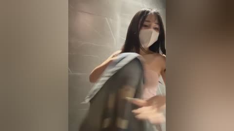 Media: A video of an Asian woman with long black hair, wearing a white face mask, blue jeans, and a white tank top, running through a dimly lit corridor with a beige wall.