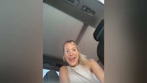 Media: A video of a smiling woman with blonde hair, wearing a sleeveless white top, sitting in a car, with the car's interior visible.