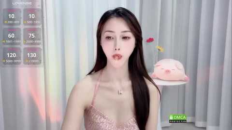 Media: Video of an East Asian woman with long, straight dark hair, wearing a pink lace camisole. Background features a white curtain, a pink plush toy, and a green text overlay.