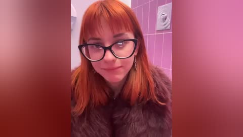 Media: Video of a fair-skinned woman with straight, vibrant orange hair and glasses, wearing a brown fur coat, in a purple-tiled bathroom with a white light switch.