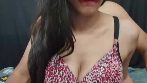 Media: A close-up video of a woman with long black hair, wearing a leopard-print bra with black straps, partially visible red lips. The background is dark.