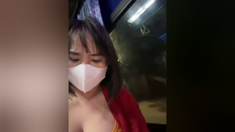 Media: A video of an Asian woman with short black hair and a white face mask, partially visible, wearing a red top, inside a dimly lit room.