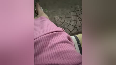 Media: A video of a person's lower body in a pink ribbed sweater, sitting on a yellow and black patterned cushion with a spiderweb design on the wall.