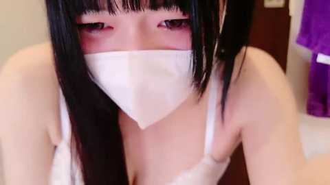 Media: Video of an East Asian woman with long black hair, wearing a white mask, revealing her face partially, and a white bra. Background shows a purple shirt and a brown door.