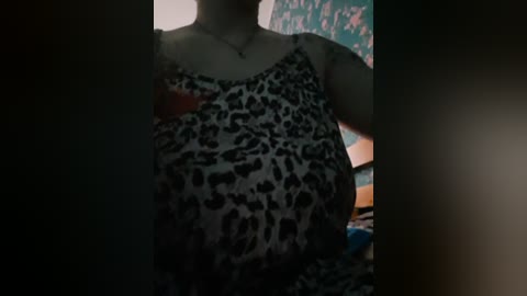 Media: Video of a woman with light skin, wearing a leopard print dress, standing in a dimly lit room with a colorful wall and a blurry background.