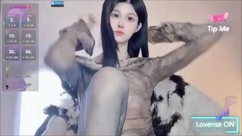 Media: A video of an Asian woman with long black hair, pale skin, and a slim physique, sitting on a black and white fur-covered chair. She wears a beige jacket. The background shows a game interface with health bars and a \"Tip Me\" button.