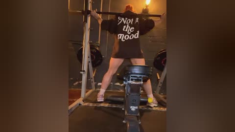 Media: Video of a muscular woman in a dark room, lifting a barbell with a black t-shirt that reads \"Not a day goes by\" in white text.