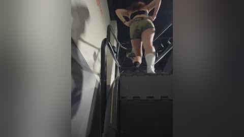 Media: A video of a woman in camouflage shorts and a black sports bra climbing a metal ladder in a dimly lit room, with a blurred silhouette of a person in the background.