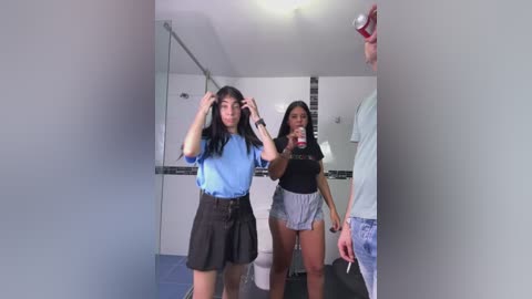 Media: Video of two young Asian women in casual clothes, one with long hair, adjusting her hair in a bathroom mirror, while the other holds a phone.