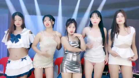 Media: Video of five East Asian women in revealing, see-through outfits; three wear white, two wear metallic silver, against a minimalist backdrop with red chairs.