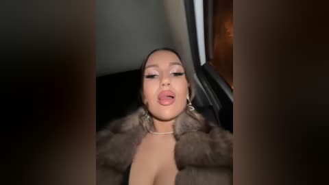 Media: A video of a woman with medium brown skin, wearing a fur coat and makeup, sticking her tongue out while seated in a car.