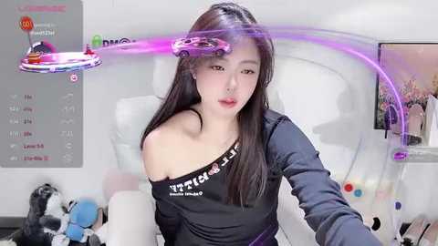 Media: Video of an East Asian woman with long black hair, wearing a black off-shoulder top, sitting in a white chair. She has a purple laser pointer on her forehead. Background shows a calendar and a gaming setup.