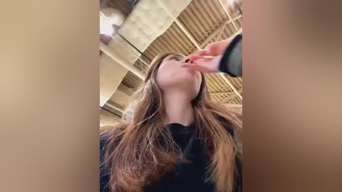 Video of a young woman with long brown hair, wearing a black top, being kissed passionately by a man in a dark shirt. Background features industrial ceiling and lighting.