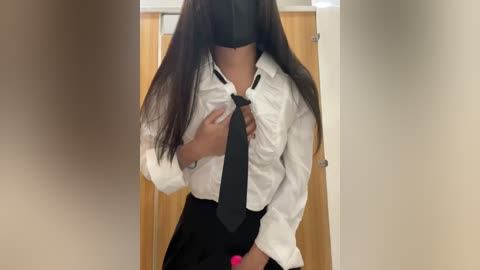 Media: Video of a woman with long, straight black hair, wearing a white button-up shirt, black tie, and black skirt. She stands in a doorway, partially obscuring her face with a black mask.