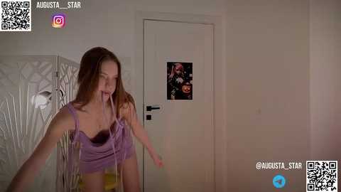 Media: A video captures a young woman in a purple crop top and black bra, seemingly startled, in a dimly-lit room with a white door adorned with a \"Halloween\" poster.