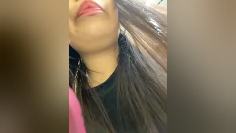 Media: A close-up video of a woman with medium brown skin and long, straight black hair, wearing a black top, captured from an upward angle, focusing on her face and hair.