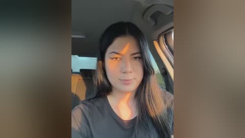 Media: Video of a young woman with long black hair and light skin, wearing a black top, seated in a car. The background shows car interior with beige and gray colors.