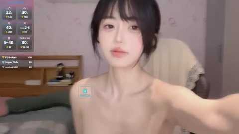 Media: A young, slender East Asian woman with straight black hair, pale skin, and small breasts, taking a topless selfie in a dimly lit bedroom with pink walls.