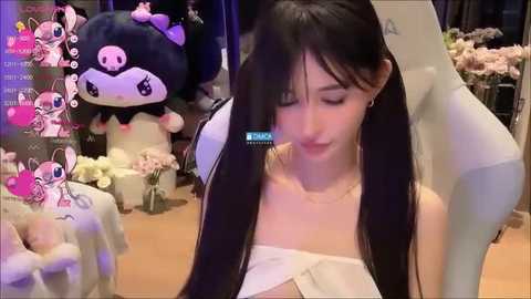 Media: A video of an Asian woman with long black hair, wearing a white strapless dress, standing in a room filled with plush toys and flowers.