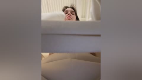 Media: A video shows a man's face peering through a window frame, with a blurred, white curtain in the foreground. The background reveals a radiator and a white wall, suggesting a domestic interior.