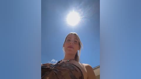 Media: Video of a blonde woman with fair skin, wearing a brown leather jacket, looking up at a bright, sunlit sky.