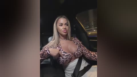 Media: Video of a blonde woman with fair skin, wearing a leopard print top and white skirt, seated in a car.