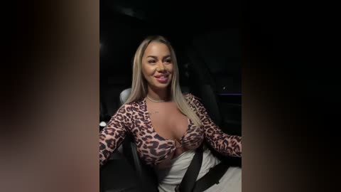 Media: Video of a smiling, curvy, blonde woman with medium skin tone wearing a leopard-print, low-cut top, seated in a black car.