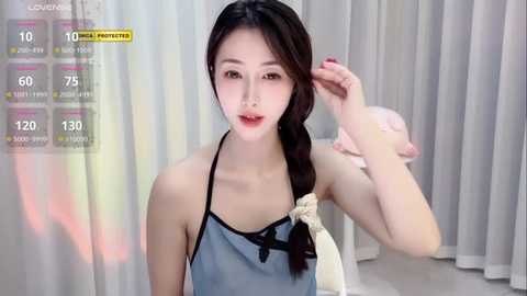 Media: Video of an Asian woman with fair skin and long black hair, wearing a blue apron, adjusting her hair. Background shows soft, pastel-colored curtains. Text overlays show \"Live Stream\" and viewer stats.