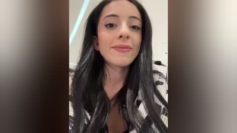 Media: Video of a young woman with long, straight black hair, wearing a black-and-white striped shirt, against a blurred, light-colored background.