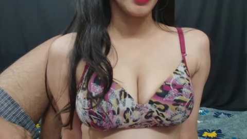 Media: Video of a young woman with light skin, long dark hair, and wearing a colorful leopard-print bra with red straps. She has a slim build and her face is partially visible with bold red lipstick.