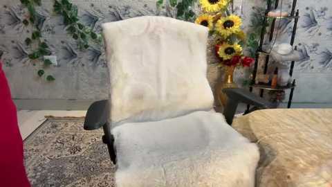 Media: Video of a recliner chair with a fluffy white blanket, surrounded by a decorative rug, sunflowers, and a black metal shelf with bottles in a cozy, vintage-style room.