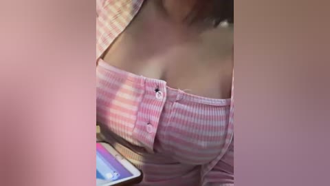 Media: Video of a light-skinned woman wearing a pink and white striped off-shoulder top, showcasing cleavage. Her hair is dark and partially visible. Background includes a laptop and blurred objects.