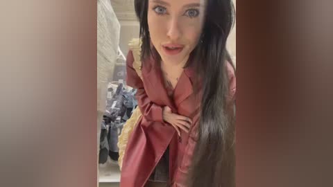 Media: Video of a woman with long black hair and pale skin, wearing a red satin robe, standing in a cluttered storage room with boxes and hanging clothes in the background.