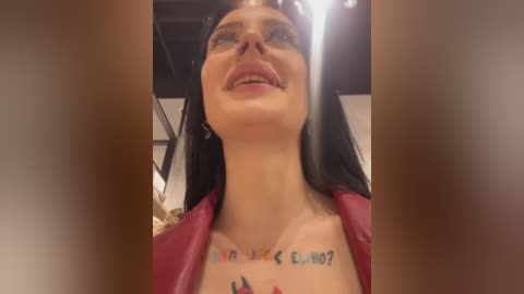 Media: A video of a smiling woman with long black hair, wearing a red jacket, and a tattoo on her neck, taken from a low angle.