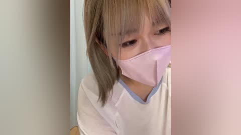 Media: A close-up video of an Asian woman with light brown hair, wearing a pink surgical mask and a white lab coat, partially obscured by a pink filter.