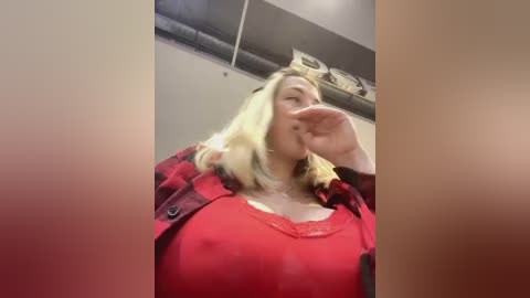 Media: Video of a blonde woman in a red top, drinking from a glass, with a blurred background of pipes and tiles.