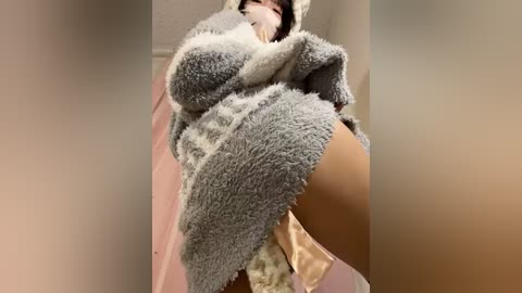 Media: A low-angle video of a woman in a gray, fluffy, hooded animal costume, with beige underwear visible, standing in a dimly lit, beige-walled room.