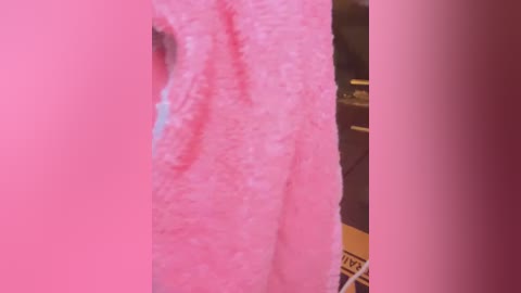 Media: Video of a pink fabric with a soft, textured surface, partially covering a dark object, possibly a piece of furniture or a bookshelf, with the edge of a cardboard box visible.