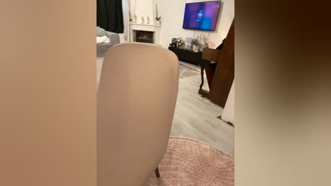 Media: Video of a cozy living room with a beige armchair, a TV displaying a blue screen, a white fireplace, and a pink blanket.