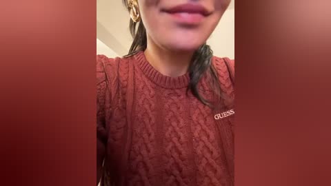 Media: A close-up video of a woman with medium skin tone, wearing a red knitted sweater with a Gucci logo. Her dark hair is pulled back, and she has a slight smile.