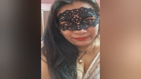 Media: Video of a smiling woman with long black hair, wearing a black lace masquerade mask covering her eyes, with fair skin and red lipstick.